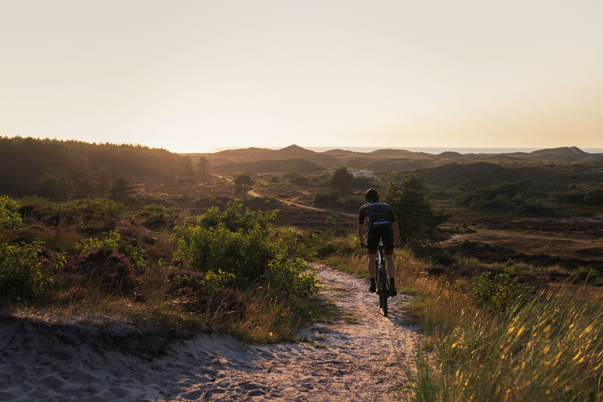 Mountainbiker over de mountainbikeroute in de Schoorlse Duinen met ondergaande zon